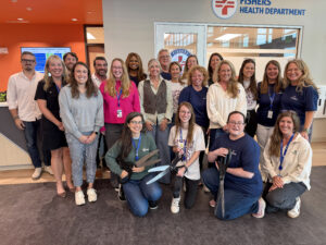 Group of adults posing together in a health department lobby, some with lanyards, smiling at the camera.